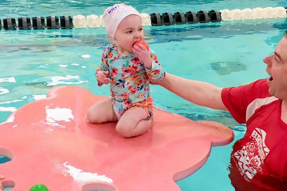 baby on lily pad in pool with swim teacher