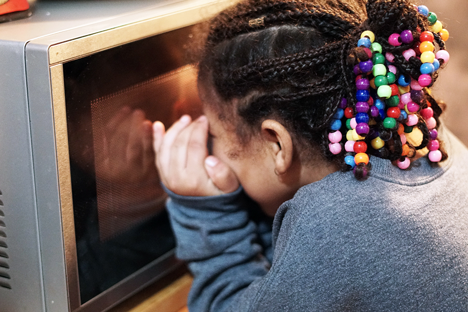 Girl peeks into microwave to check on a mug cake.