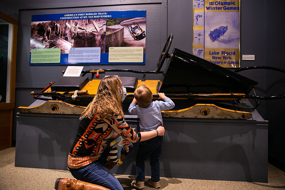 Things to do in Lake Placid with Kids: The Olympic Museum Mom and son looking at exhibit Things to Do in Lake Placid on a Winter Vacation Status message