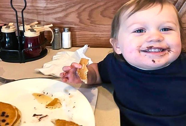 Photo of child eating pancakes and smiling with food on their face.
