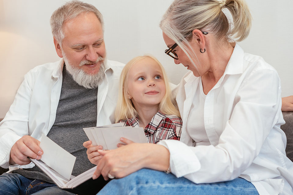 child sitting with grandparents looking through photos 101 Questions To Ask Grandparents About Their Lives