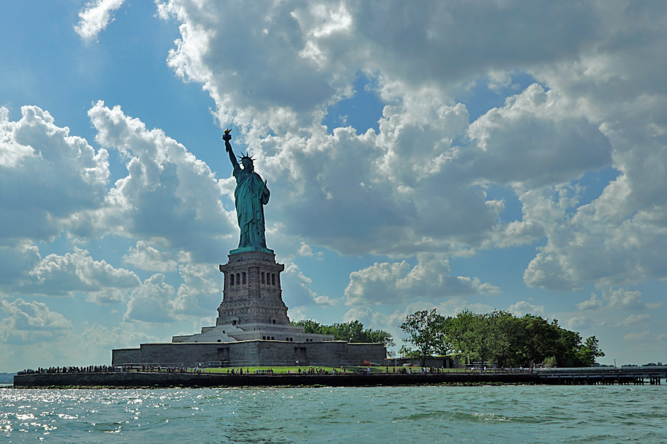 Lady Liberty in New York Harbor on a blue sky day one of our favorite NYC tourist attractions